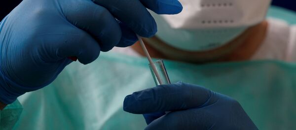 Francuski lekar, u zaštitnom odelu i sa maskom na licu, drži epruvetu - Sputnik Srbija