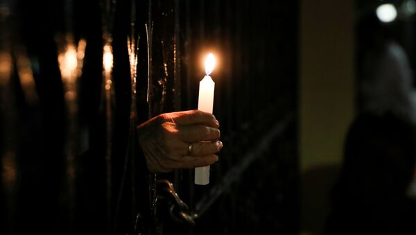 Верник држи свећу кроз ограду у цркви која је затворена због санитарних мера у Сантјагу, Чиле, 3. априла 2021. - Sputnik Србија