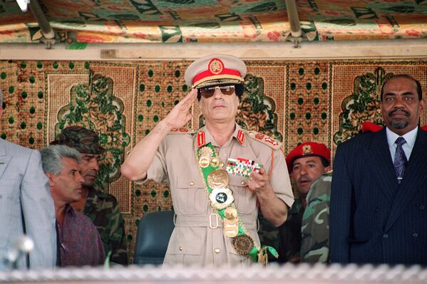 Либијски вођа пуковник Муамер ел Гадафи поздравља трупе током војне параде 1. септембра 1994. године у Триполију, поводом прославе 25 година од доласка на власт. Гадафи је 1969. године извео пуч без крви, који је свргнуо краља Идриса, док је монарх био ван земље. Десно од Гадафија стоји судански вођа Омар Ал-Башир. - Sputnik Србија