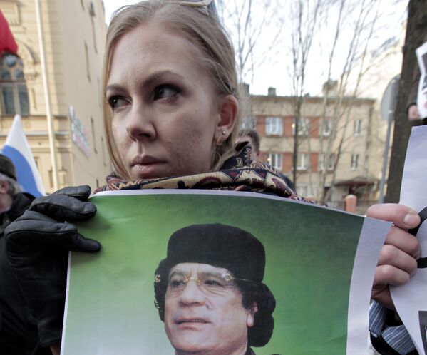 Учесница акције протеста против иностране инвазије на Либију стоји испред Генералног конзулата САД у Санкт Петербургу са портретом Гадафија у рукама. - Sputnik Србија