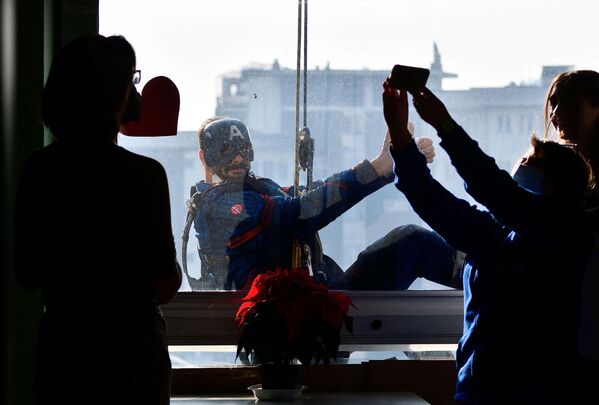 Čovek obučen kao Kapetan Amerika pozira za najmlađe ispred prozora pedijatrijskog odeljenja. - Sputnik Srbija