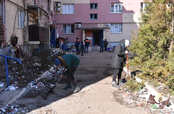Lokalni stanovnici čiste smeće u dvorištu stambene zgrade oštećene granatiranjem u Volnovahi - Sputnik Srbija