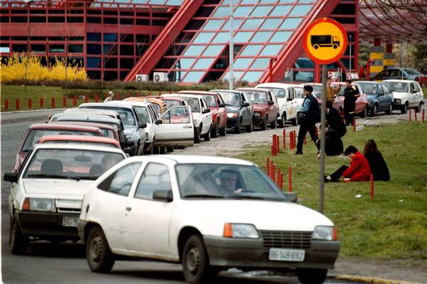 Возачи се одмарају поред паркираних аутомобила у бескрајним редовима испред београдских бензинских пумпи у среду, 24. марта 1999. Након што је НАТО објавио да је спреман да покрене казнене ваздушне нападе након што је Београд одбацио споразум за Косово који је спонзорисала међународна заједница, бензин је преусмерен на војне потребе са ограниченим залихама за општу популацију. - Sputnik Србија