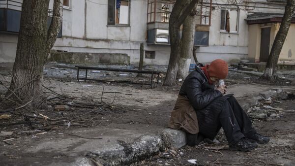 Žena sedi na ulici pored uništenih zgrada u Rubežnom u Donbasu - Sputnik Srbija