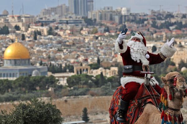 Palestinac obučen kao Deda Mraz, pozira dok jaše kamilu na Maslinovoj gori u Jerusalimu. - Sputnik Srbija