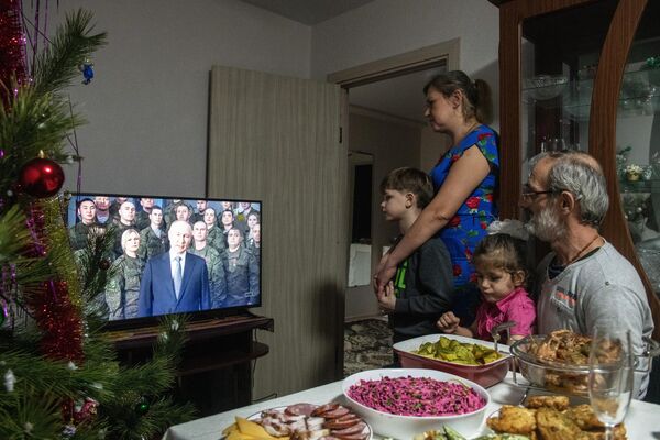 Porodica gleda prenos novogodišnjeg obraćanja ruskog predsednika Vladimira Putina tokom proslave Nove 2023. godine u Marijupolju. - Sputnik Srbija