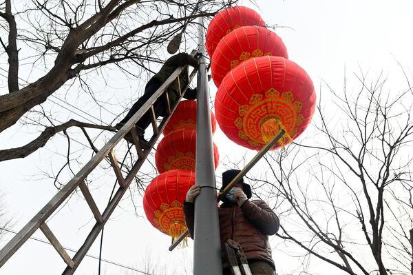 Radnici kače crvene fenjere na rasvetni stub duž ulice za predstojeću proslavu kineske lunarne Nove godine u Pekingu 14. januara 2023. - Sputnik Srbija