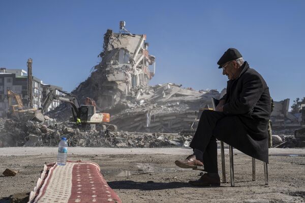 Mehmet Nasir Duran, 67, sedi na stolici, dok teške mašine uklanjaju krhotine sa zgrade, gde je pet članova njegove porodice zarobljeno u Nurdagiju, na jugoistoku Turske - Sputnik Srbija
