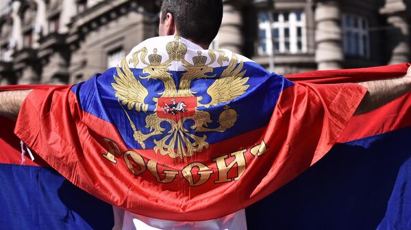 Mladić ogrnut ruskom zastavom dok u rukama drži srpsku zastavu - Sputnik Srbija