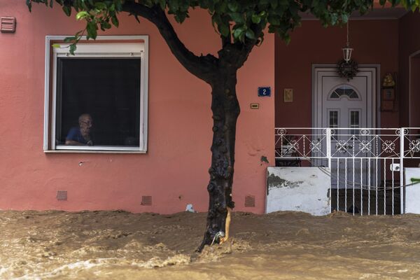 Мештанин кроз прозор гледа насталу штету од поплава. - Sputnik Србија