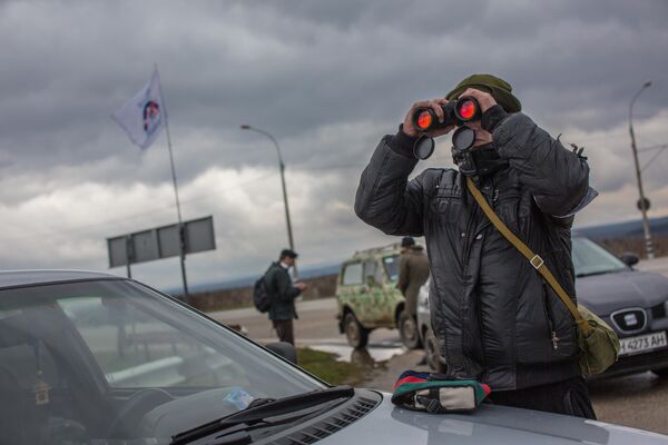 Мештанин посматра кроз двоглед војни контролни пункт на улазу на аеродром „Белбек“ код Севастопоља. - Sputnik Србија