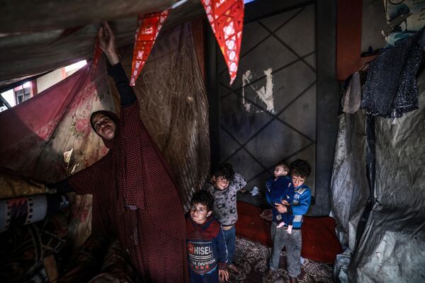 Palestinka popravlja krov unutar improvizovanog šatora dok deca posmatraju kamp pored ulice u Rafi 14. marta 2024. - Sputnik Srbija