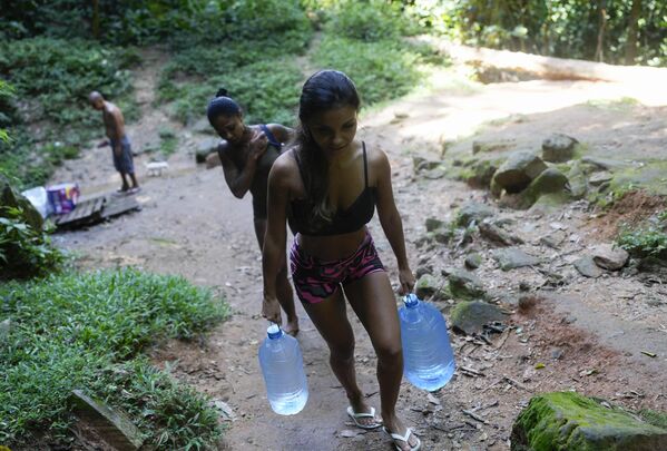 Žena nosi flaše vode za piće nakon što ih je natočila uplaninama u faveli Rosinha u Rio de Žaneiru, Brazil, ponedeljak, 18. mart 2024. - Sputnik Srbija