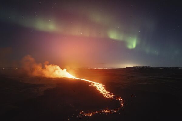 Поглед на лаву која тече из вулкана у позадини северног светла, у близини града Гриндавик на Исланду. - Sputnik Србија