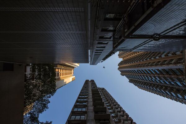 на фоткографији се види голуб који лети међу стамбеним зградама у Хонгконгу. - Sputnik Србија