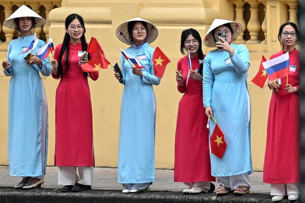 Žene u tradicionalnim vijetnamskim haljinama „Ao Dai“ mašu vijetnamskom i ruskom nacionalnom zastavom dok čekaju dolazak ruskog predsednika Vladimira Putina ispred Predsedničke palate u Hanoju - Sputnik Srbija