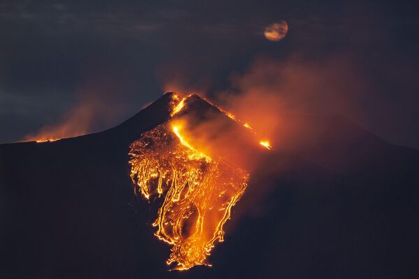 Mesec se delimično vidi na nebu dok lava teče iz vulkana Etna, u blizini Katanije na Siciliji. - Sputnik Srbija