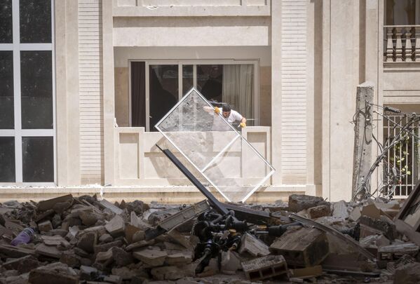 Иранац уклања рушевине из свог оштећеног стана који се налази испред зграде која је уништена у израелским нападима у стамбеној зони у западном Техерану. - Sputnik Србија