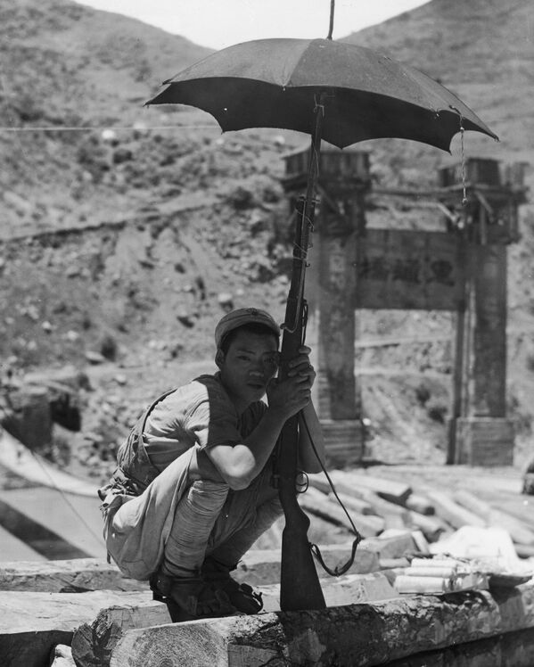 Mladi kineski vojnik čuči u hladu suncobrana pričvršćenog za pušku dok čuva stražu iznad mosta Hvitung, u Burmi, 1944. godina. Kineski vojnici su pokušali da sa saveznicima oslobode Burmu nakon što su je japanske trupe zauzele 1942. godine. Žestoke borbe su se sporadično nastavile u gerilskim napadima tokom naredne dve godine, sve dok britanske i kineske snage nisu postepeno ponovo uspostavile kontrolu nad zemljom 1945. godine. - Sputnik Srbija