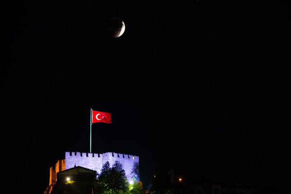 Делимично помрачење Месеца видљиво је на небу изнад турске заставе која се вијори на осветљеном замку Анкара у Анкари, Турска. - Sputnik Србија