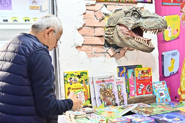 Maketa dinosaurusa na jednom od štandova sa knjigama i slikovnicima posvećenim najmlađima i deka koji bira poklon kojim će obradovati svog unuka ili unuku - Sputnik Srbija