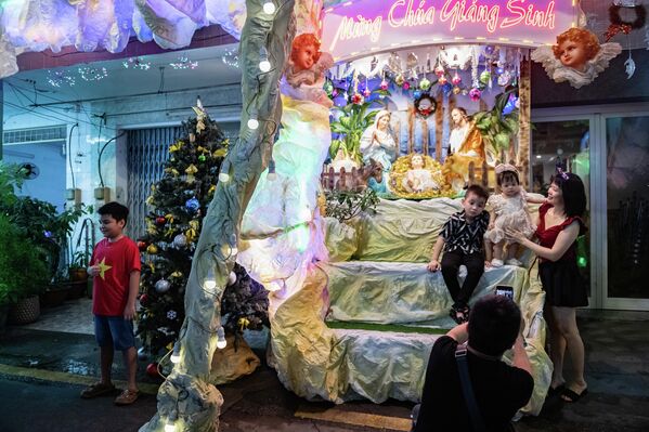 Ljudi se fotografišu ispred kuće ukrašene jaslicama na Badnje veče u Ho Ši Minu, u Vijetnamu. u toj zemlji Božić nije državni praznik, ali ga mnogi ljudi obeležavaju kao svečanu priliku. U katoličkim zajednicama, stanovnici ukrašavaju uske uličice u kojima žive svetlima, jaslicama i verskim simbolima. Tokom božićne sezone, ove uličice postaju zajednički praznični prostori i privlače posetioce iz drugih krajeva. - Sputnik Srbija