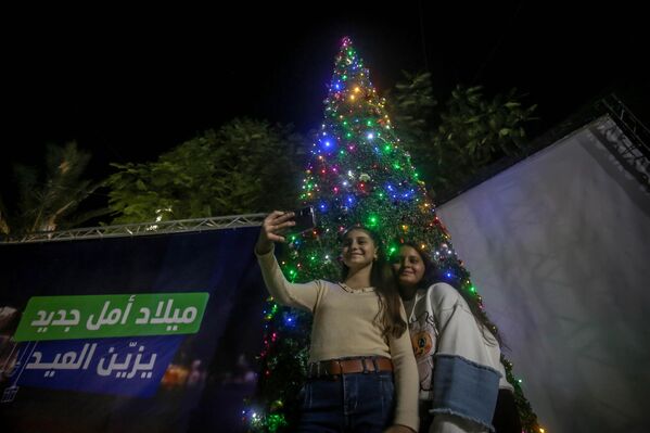 Ljudi poziraju ispred božićne jelke dok hrišćani koji žive u Gazi prisustvuju božićnoj misi u Latinskoj crkvi (Crkva Svete porodice) u Gazi. - Sputnik Srbija