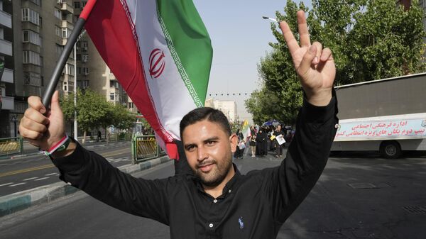 A man flashes a victory sign as he carries an Iranian flag while attending the funeral ceremony of the Iranian armed forces generals, nuclear scientists and their family members who were killed in Israeli strikes, at Azadi (Freedom) street, in Tehran, Iran, Saturday, June 28, 2025.  - Sputnik Србија