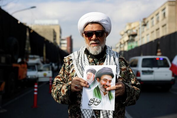Човек држи транспарент са сликом новог врховног вође Ирана, Моџтабе Хамнеја, заједно са покојним врховним вођом ајатолахом Алијем Хамнејом, на скупу подршке новом врховном вођи. - Sputnik Србија