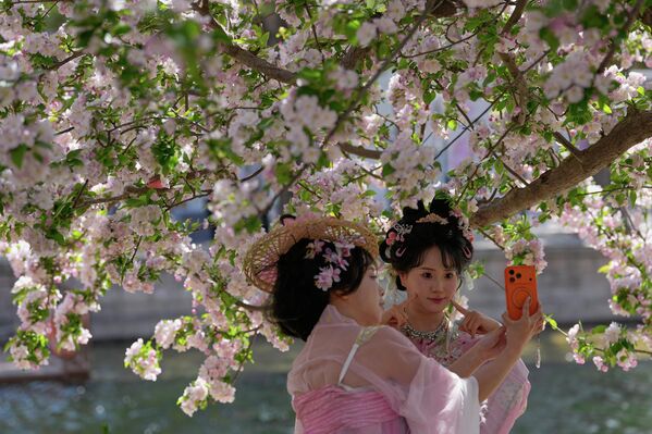 Жене у традиционалним ношњама праве селфије са цветовима трешње дуж обале реке у јавном парку током сезоне пролећног цветања, у Пекингу, у недељу, 5. априла 2026. године. - Sputnik Србија