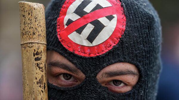 Čovek sa maskom koji nosi palicu i antinacistički amblem tokom protesta protiv vlasti u Čileu - Sputnik Srbija