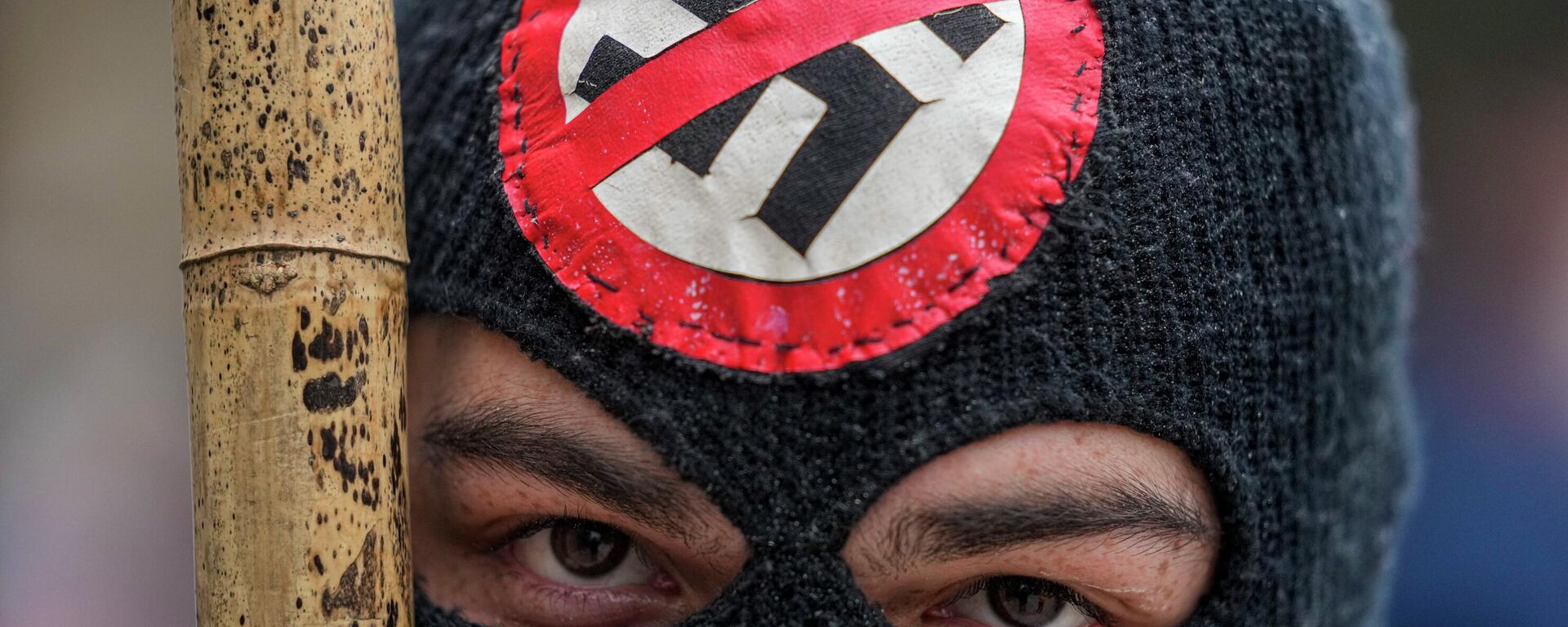Čovek sa maskom koji nosi palicu i antinacistički amblem tokom protesta protiv vlasti u Čileu - Sputnik Srbija, 1920, 07.04.2026