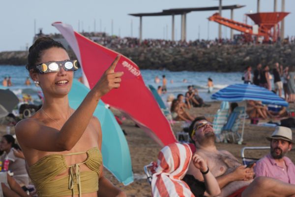Posetilac plaže, sa specijalnim naočarima za posmatranje pomračenja, pokazuje prema nebu uoči delimične faze pomračenja Sunca na plaži Puerto de Sagunto, u blizini Valensije. - Sputnik Srbija