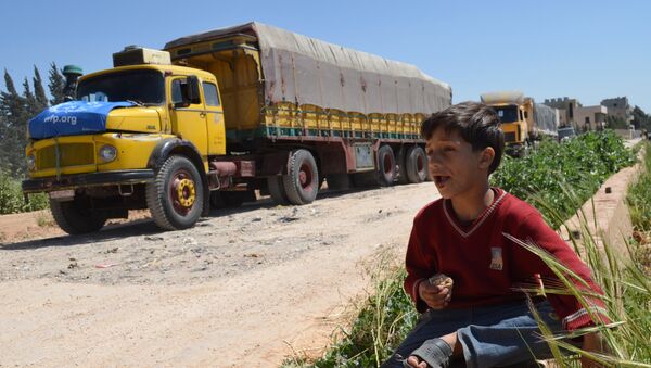 Сиријски дечак једе док поред њега пролази конвој камиона Светског програма за храну и Уницефове међународне помоћи у околини града Хомса, 21. април 2015. - Sputnik Србија