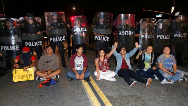 Demonstranti sede ispred policije tokom protesta protiv Donalda Trampa u Kosta Mesi u Kaliforniji. - Sputnik Srbija