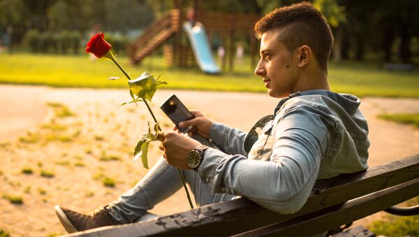 Mladić sedi na klupi držeći ružu - Sputnik Srbija