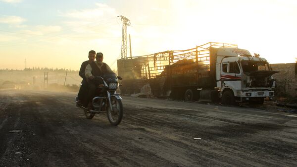 Ljudi na motoru prolaze pored oštećenog kamiona humanitarne pomoći u Urm al Kubri zapadno od sirijskog Alepa - Sputnik Srbija