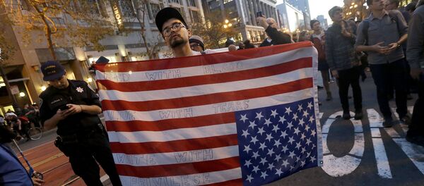 Demonstrant nosi američku zastavu naopačke tokom protesta protiv Trampa u San Francisku Demonstrant nosi američku zastavu naopačke tokom protesta protiv Trampa u San Francisku - Sputnik Srbija
