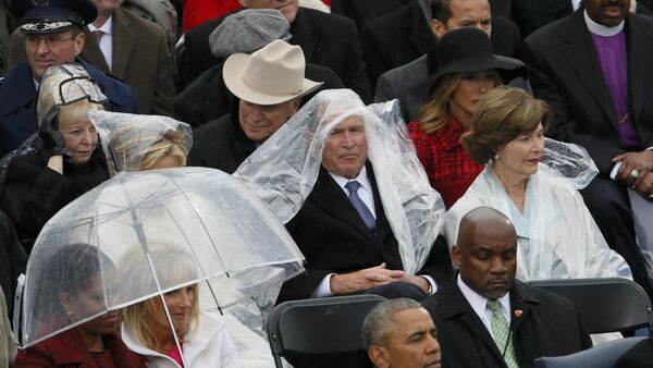 Бивши амерички председник Џорџ В. Буш штити се кабаницом од кише на церемонији инаугурације Доналда Трампа у Вашингтону - Sputnik Србија