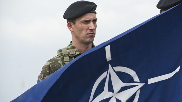 Pripadnik KFORA  Prištini pored NATO zastave - Sputnik Srbija