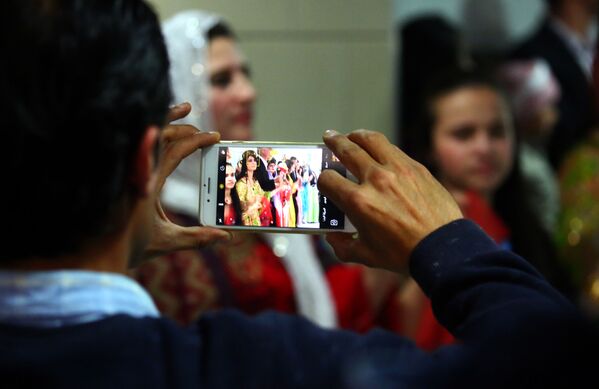 A man takes a photo on his phone of Syrian-Kurdish women modelling traditional Kurdish attire during a fashion show in the northeastern Syrian city of Qamishli on March 10, 2017, which coincides with the Day of Kurdish Clothing. - Sputnik Србија