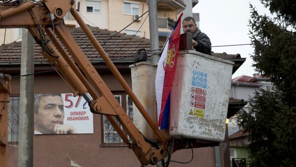 Radnik na dizalici postavlja srpsku zastvu, a u pozadini na kući se vidi fotografija ubijenog Olivera Ivanovića. - Sputnik Srbija