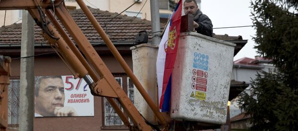 Radnik na dizalici postavlja srpsku zastvu, a u pozadini na kući se vidi fotografija ubijenog Olivera Ivanovića. Radnik na dizalici postavlja srpsku zastvu, a u pozadini na kući se vidi fotografija ubijenog Olivera Ivanovića. - Sputnik Srbija