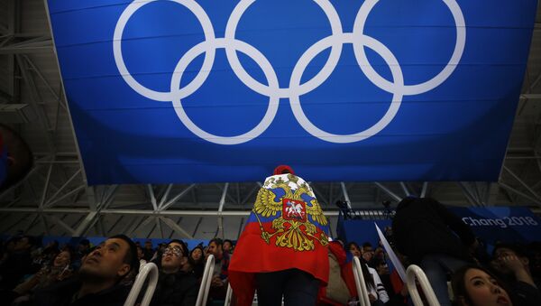 Navijač sa zastavom Rusije stoji ispod olimpijskih krugova na hokejaškoj utakmici između Rusije i Nemačke na Olimpijskim igrama u Pjongčangu - Sputnik Srbija