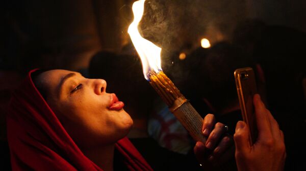 Žena pali sveće pri silasku Blagodatnog ognja u Hramu groba Gospodnjeg. - Sputnik Srbija