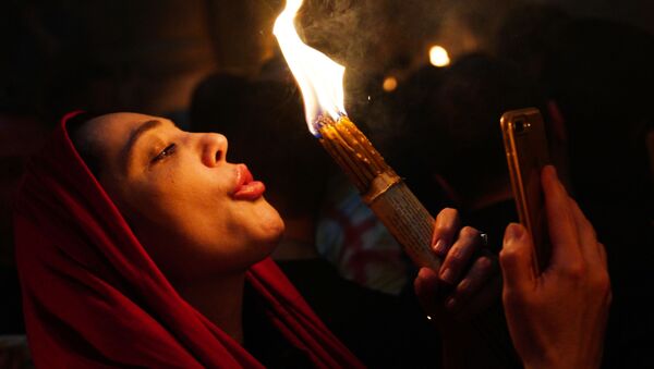 Жена пали свеће при силаску Благодатног огња у Храму гроба Господњег. - Sputnik Србија