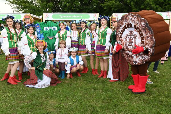 Žene i deca odeveni u kostime stoje u blizini promotivnog odbora koji predstavlja ruski region Tulu. - Sputnik Srbija