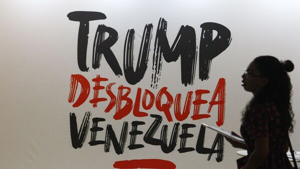 Жена пролази поред транспарента на којем на шпанском пише Трампе, деблокирај Венецуелу у Каракасу - Sputnik Србија