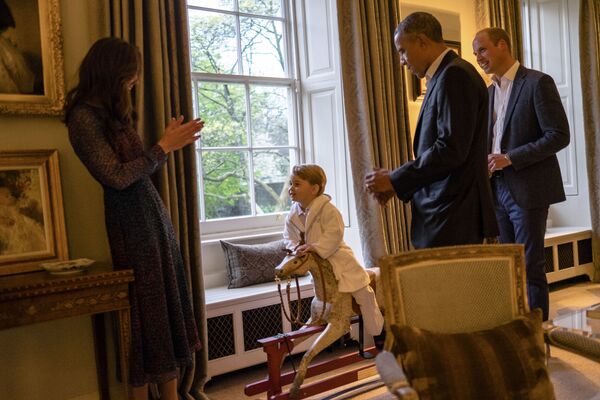 Млади принц Џорџ, трећи у реду за британски престо, на дрвеном коњу у друштву родитеља, војводе од Кембриџа и америчког председника Барака Обаме. - Sputnik Србија