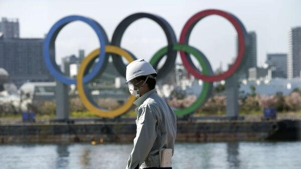 Човек с маском испред олимпијских кругова у Токију. - Sputnik Србија
